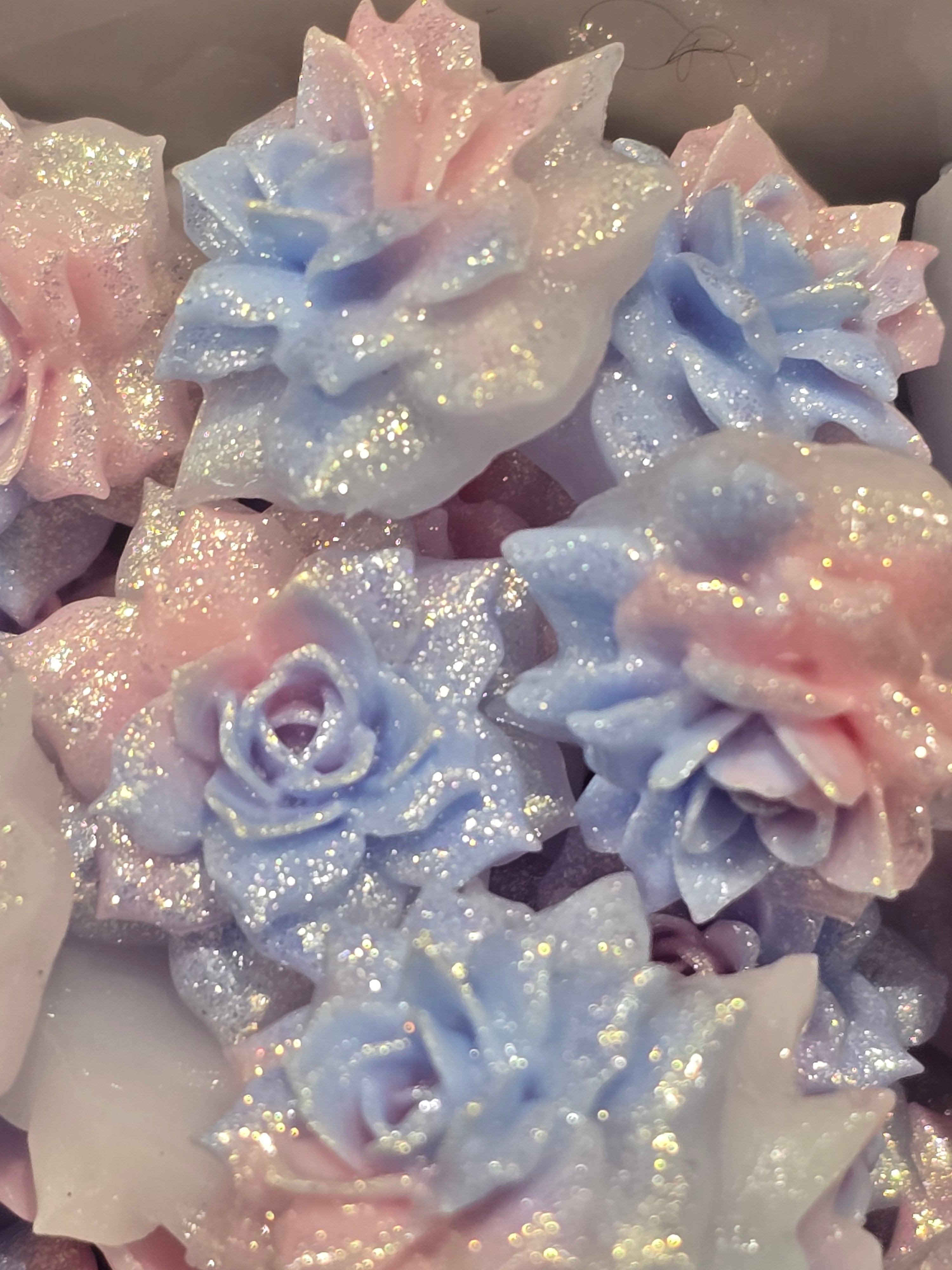 A close-up of glittery decorative soft flowers in pastel pink, light blue, and white, with sparkling holographic shimmer.