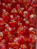 A close-up pile of round, transparent red glass beads with white floral  on their surfaces.