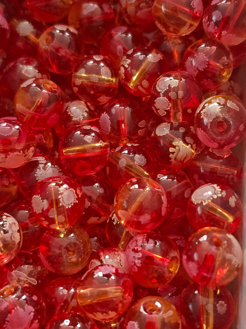 A close-up pile of round, transparent red glass beads with white floral  on their surfaces.