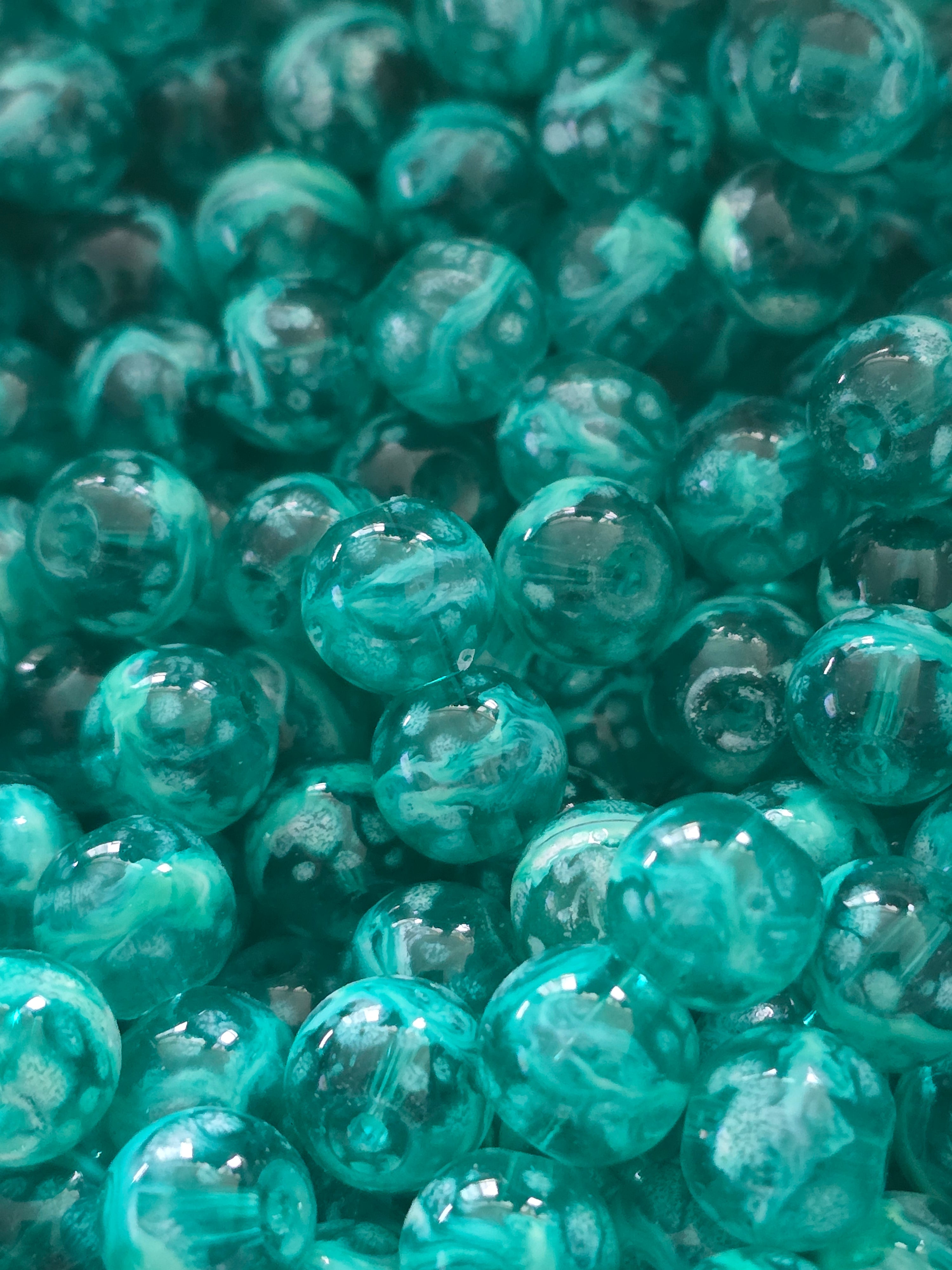 A close-up pile of translucent teal glass beads with swirling patterns inside.