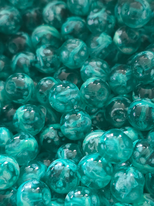 A close-up pile of translucent teal glass beads with swirling patterns inside.