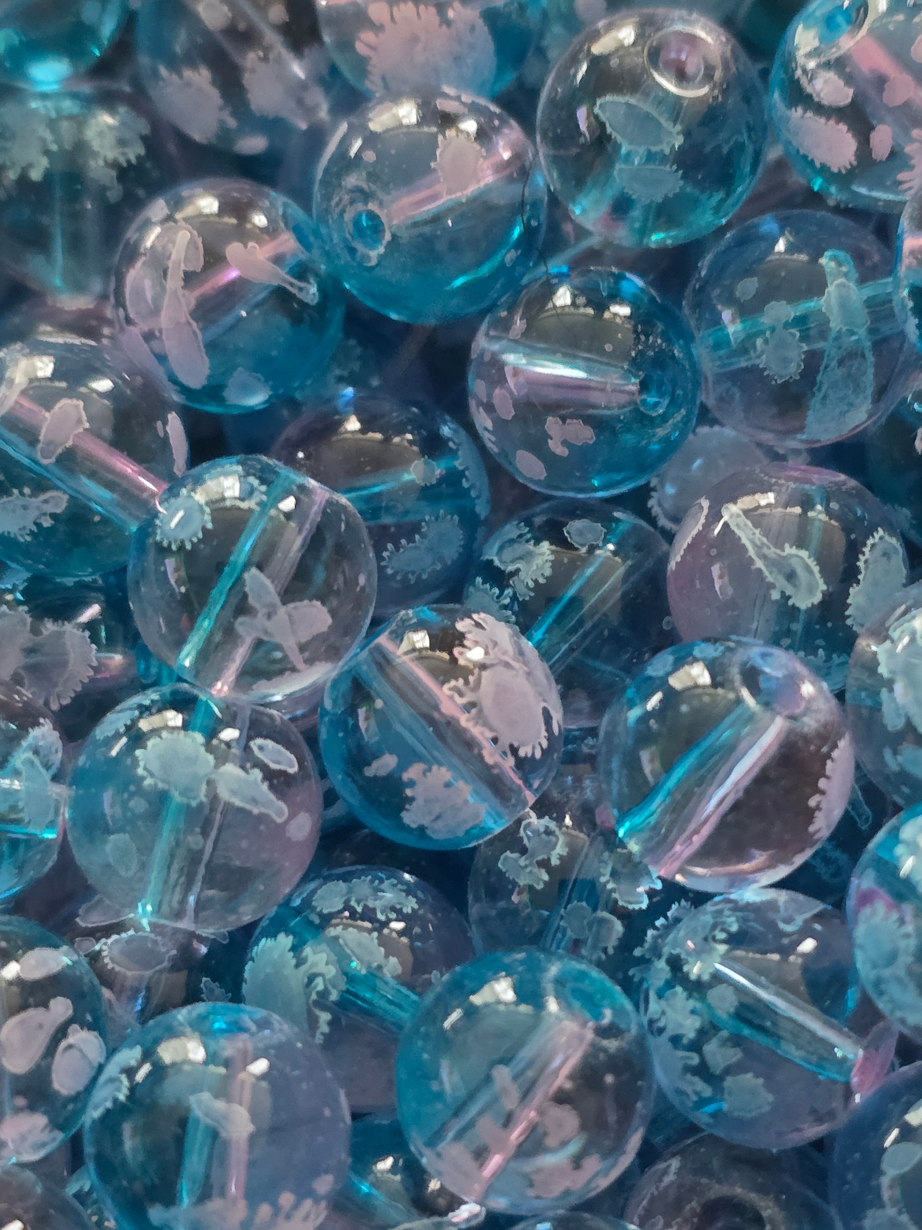 A close-up pile of round, transparent blue beads with white floral.
