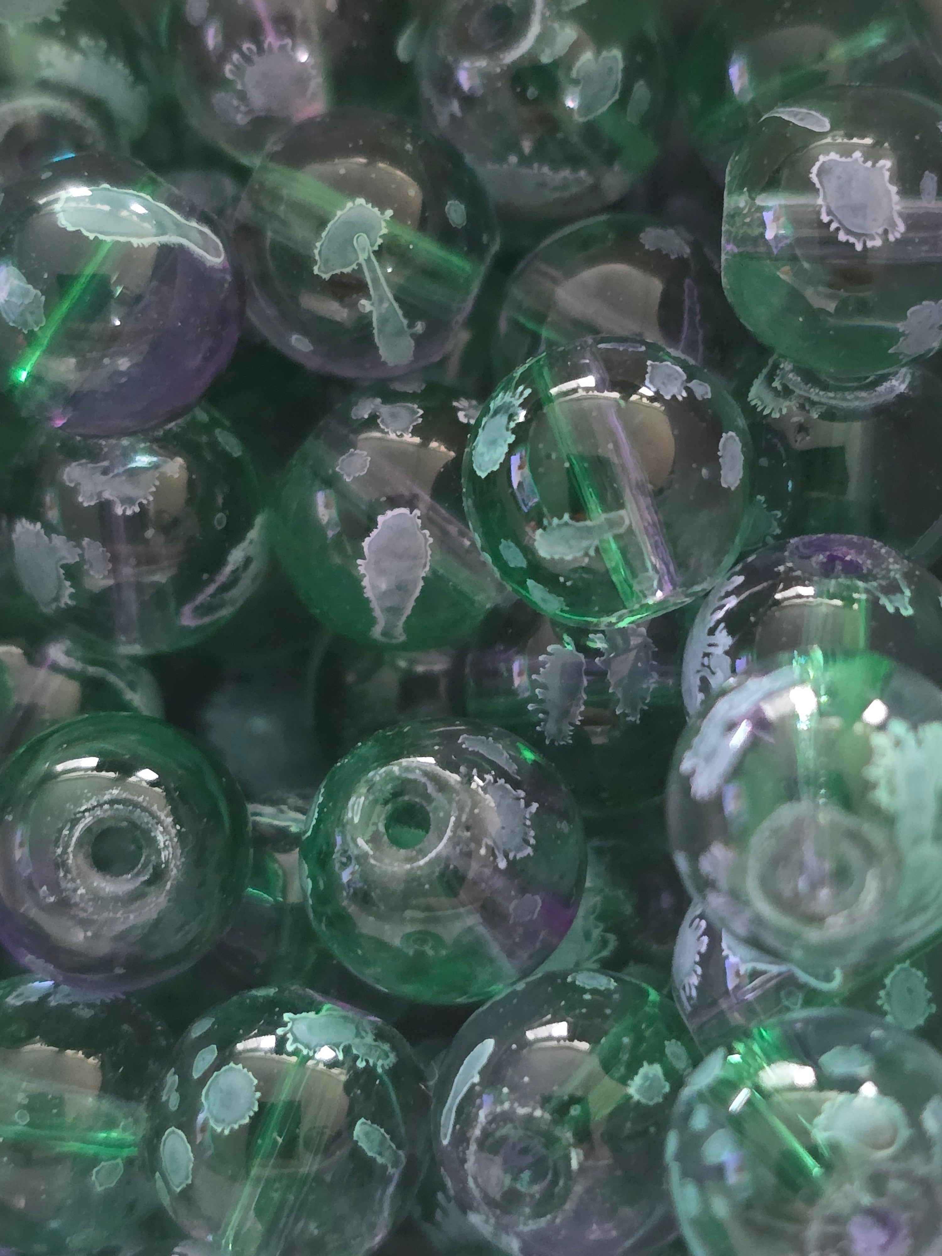 A close-up pile of round glass beads in translucent green and clear shades, showing white leaf-like inclusions on the glass.