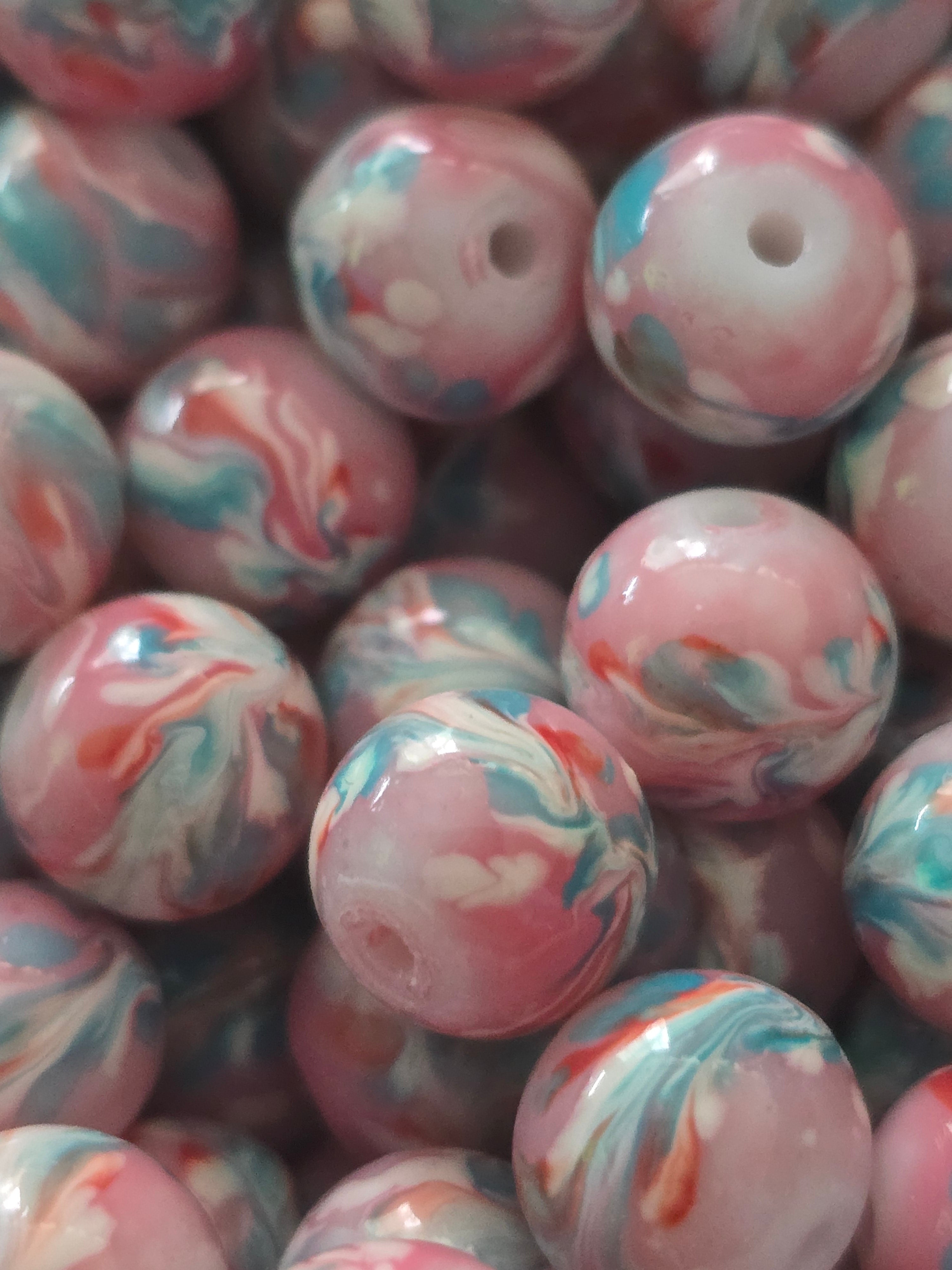 A close-up pile of round marbled glass beads in pink, white, and light blue.