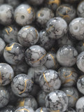 A close-up pile of round, glossy stone beads with a white and gray marbled pattern and thin gold veining.