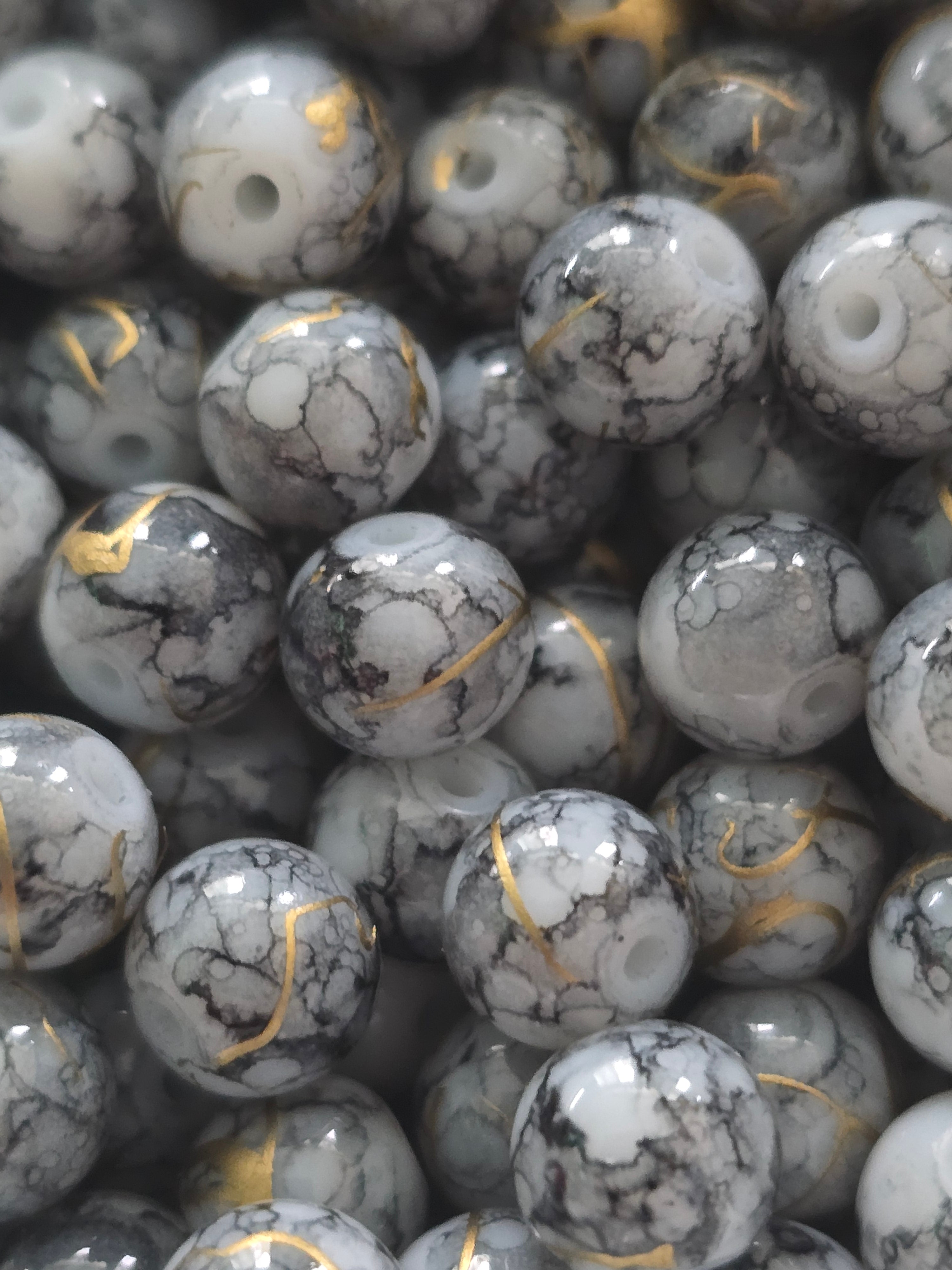 A close-up pile of round, glossy stone beads with a white and gray marbled pattern and thin gold veining.