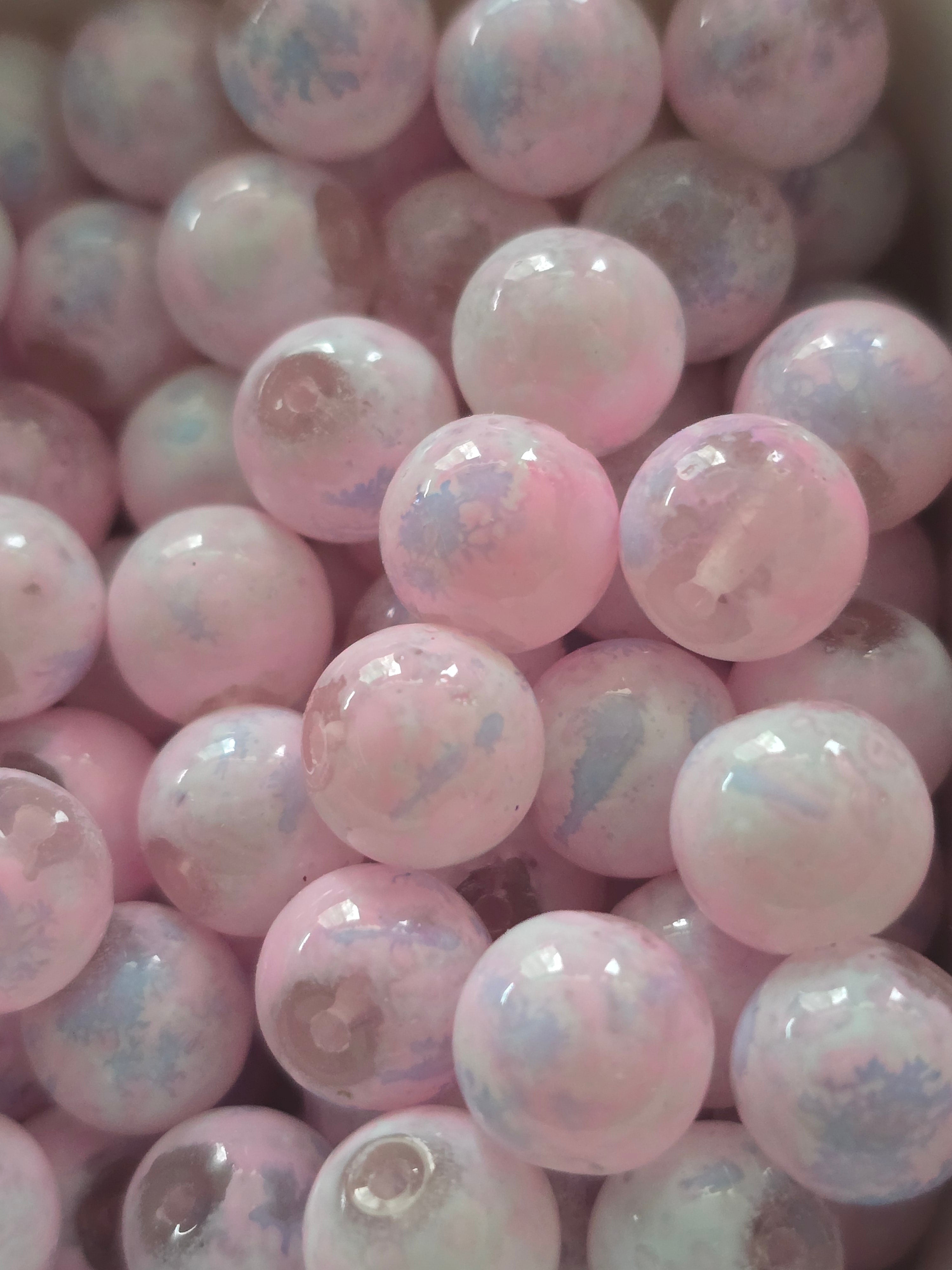 A close-up pile of round, glossy pink glass beads with white and light blue marbled inclusions.