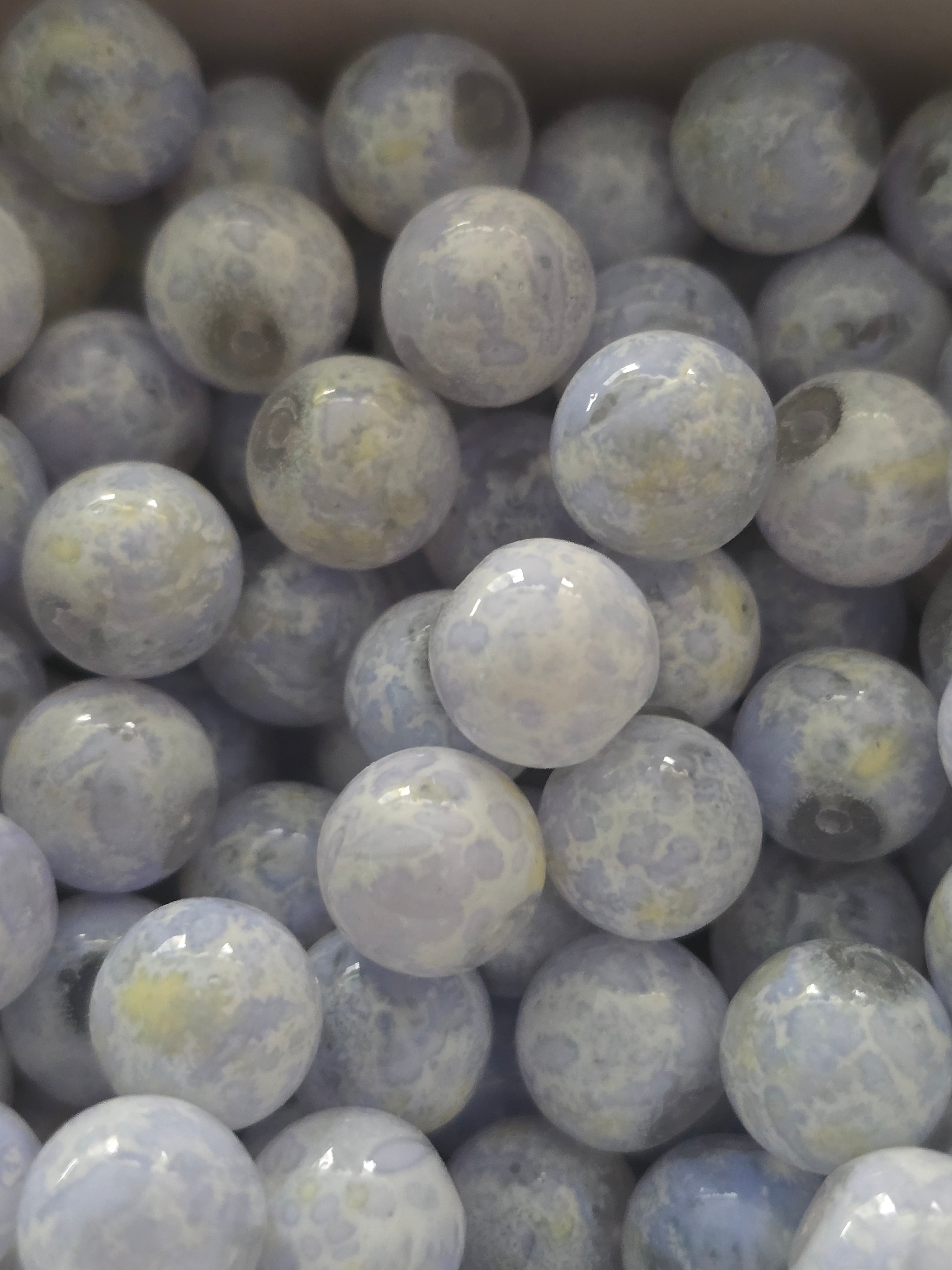 A close-up pile of round, glass beads in pale gray, white, and soft blue-gray tones with subtle marbled or cloudy inclusions.