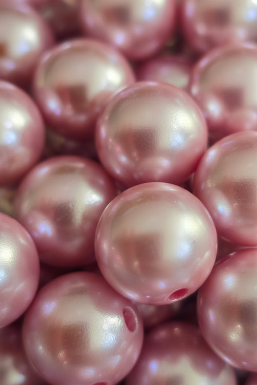 A close-up pile of glossy, iridescent pink beads with a pearlescent finish.