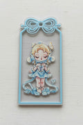 A rectangular acrylic tag featuring a  girl character in a light blue and white outfit on a dark background, with a decorative bow.