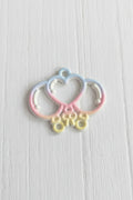 A small decorative metal charm with a pastel rainbow gradient, featuring a heart and crescent moon design with three hanging loops.
