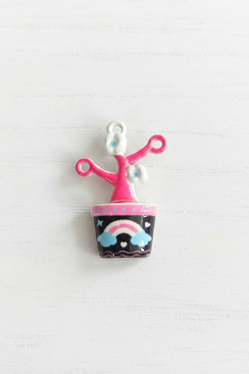 A small decorative charm with a pink looped stem, white flower details, and a dark pink cylindrical cap decorated with a rainbow.