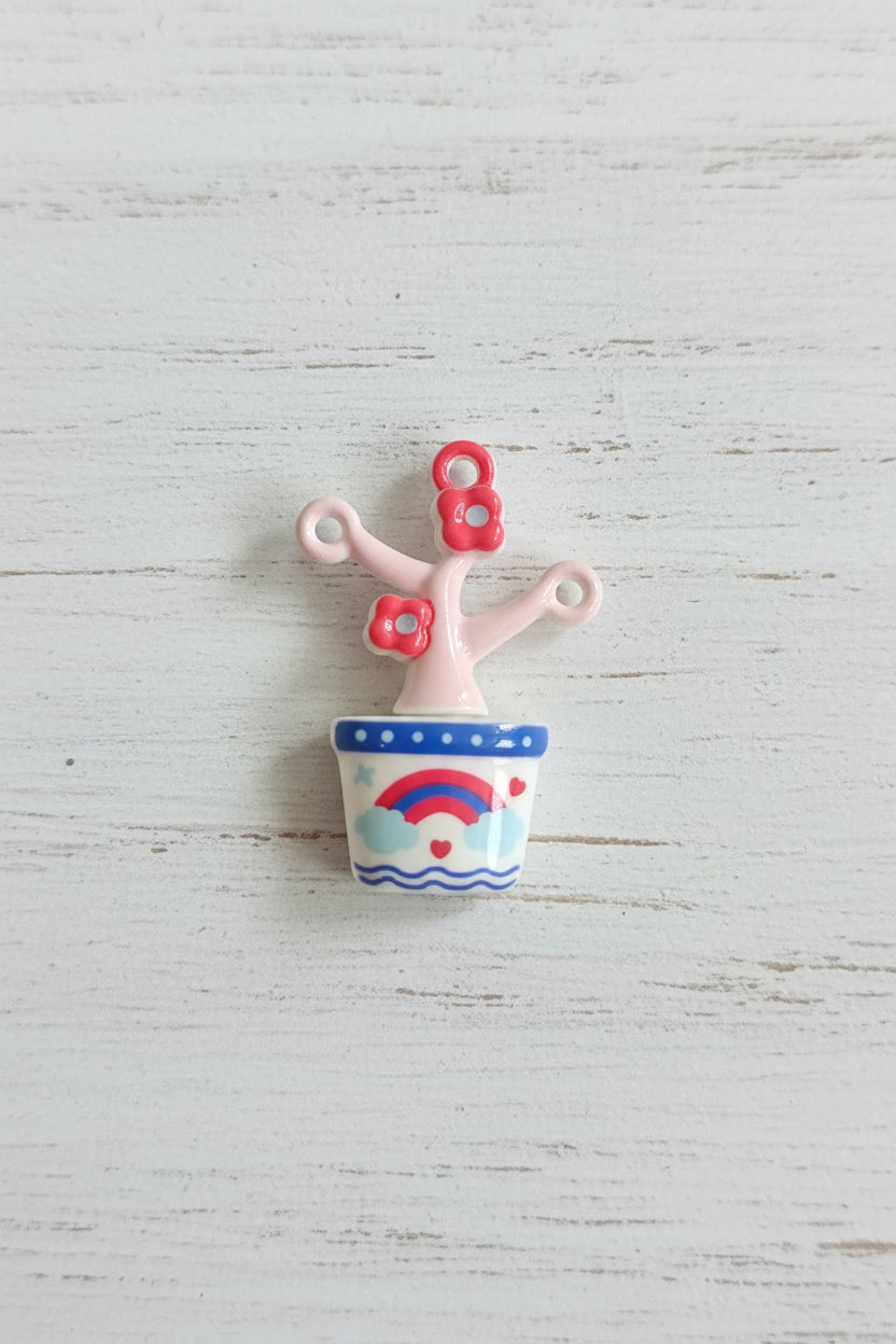A small decorative pendant with a pale pink branch-like form, two red flower shapes, and a patterned cylindrical cap in blue, white, and red.