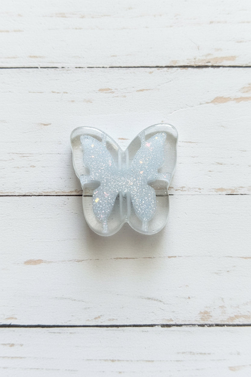 A butterfly-shaped clear resin bead filled with silver glitter.