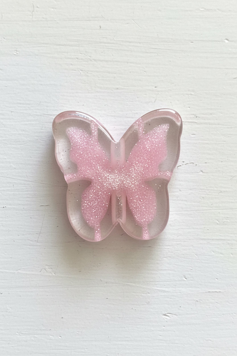 A butterfly-shaped resin bead with glittery pink wings and a clear outer border.