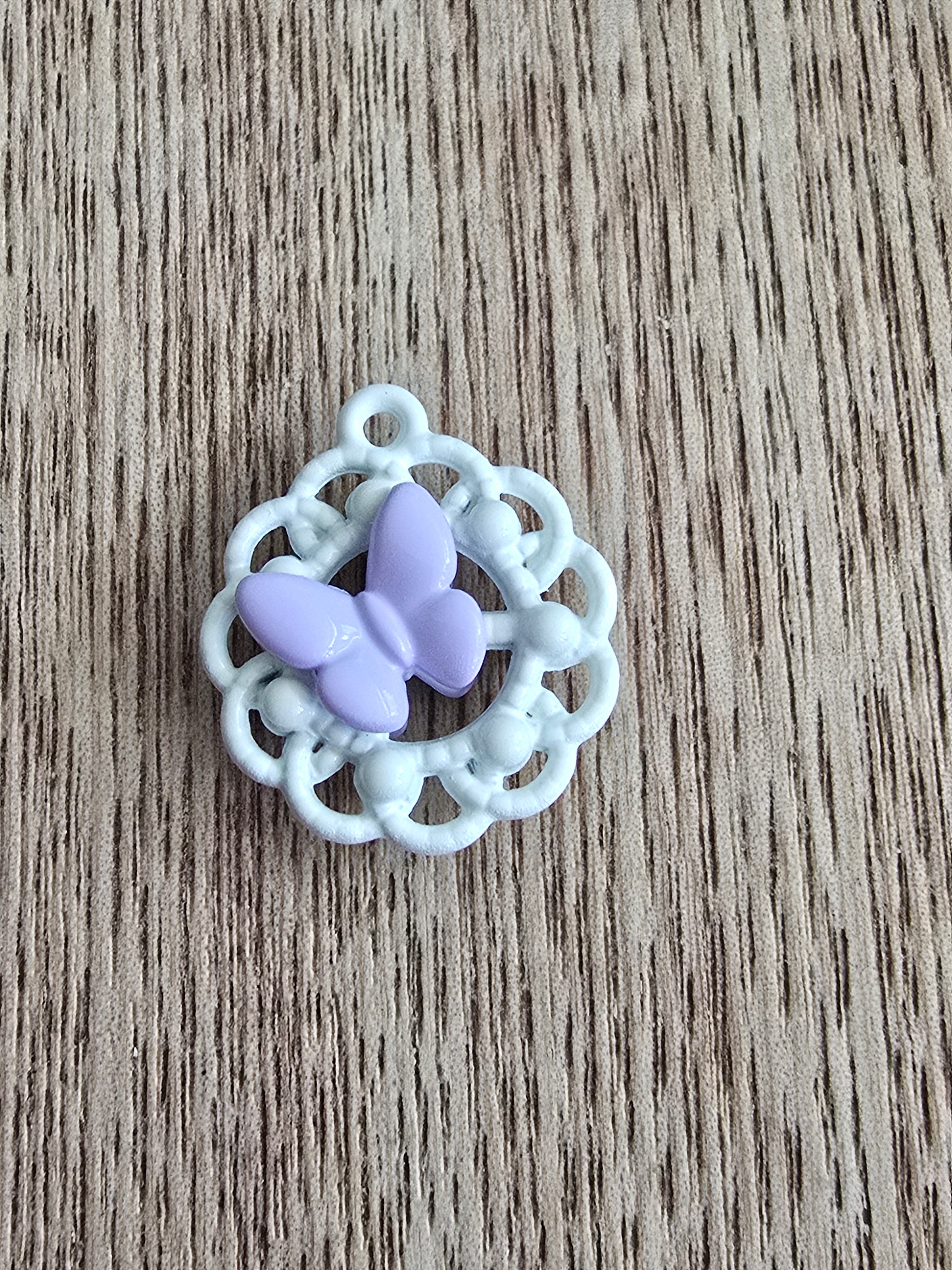 A small white metal circular lace-like pendant with a central lavender butterfly.