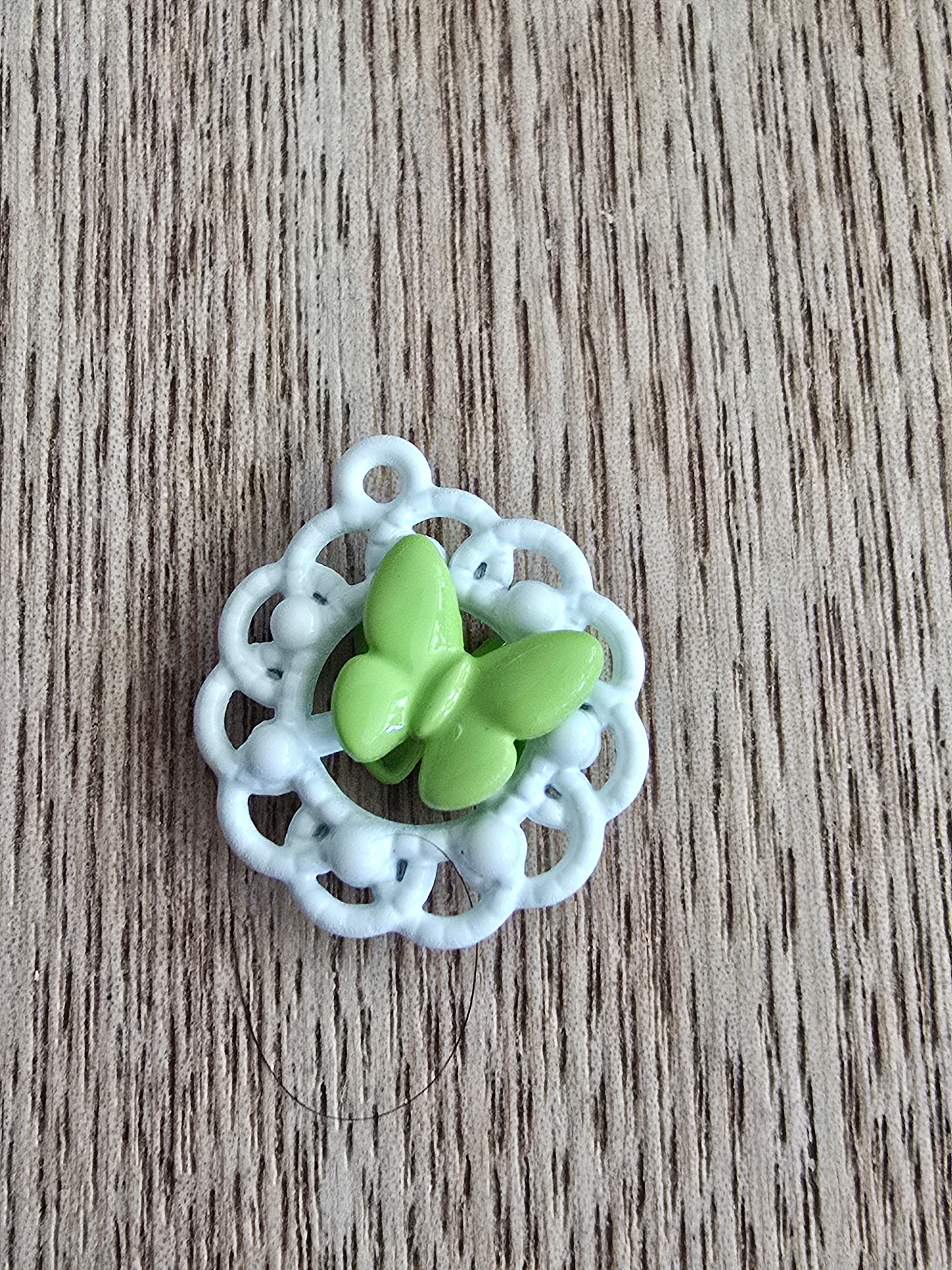 A small metal pendant featuring a glossy light green butterfly motif set within a white scalloped circular frame.
