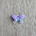 A small metal butterfly-shaped connector in lavender purple with mint green accents and white loops