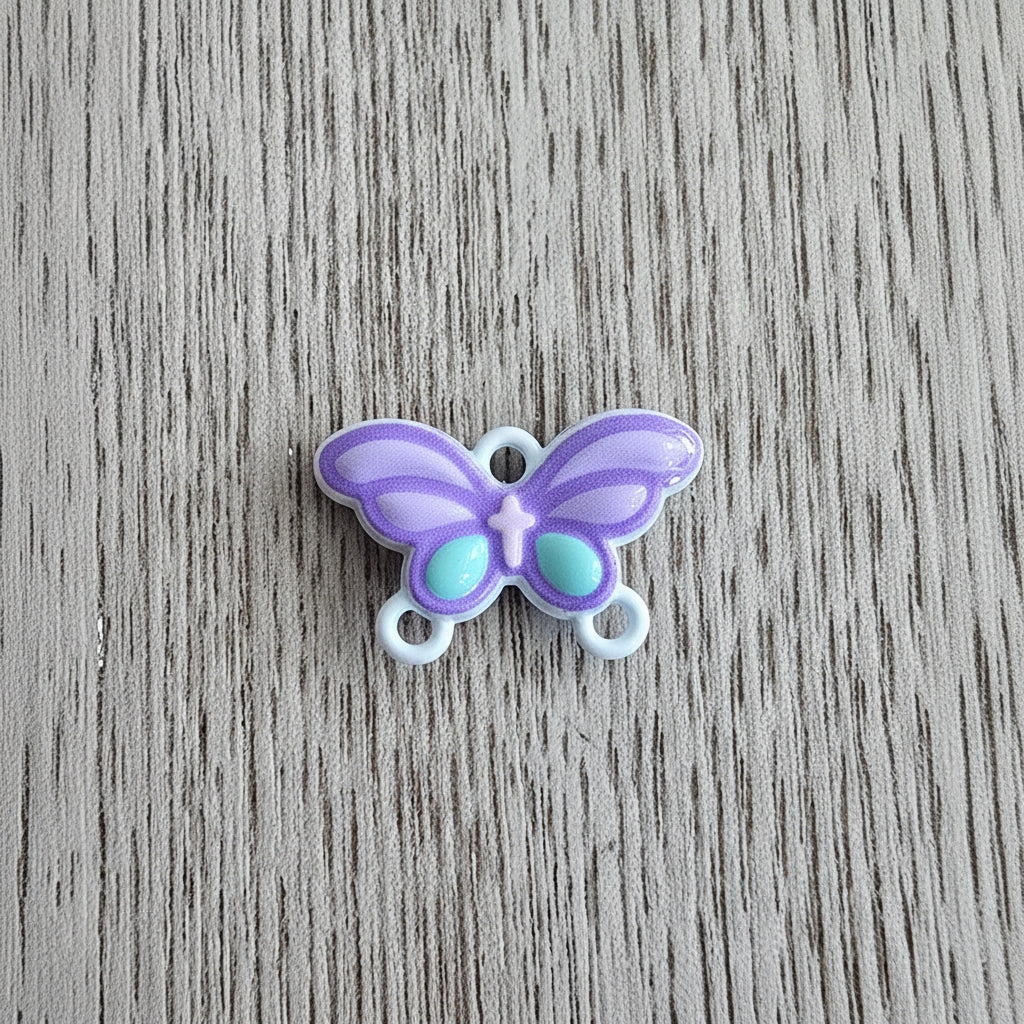 A small metal butterfly-shaped connector in lavender purple with mint green accents and white loops