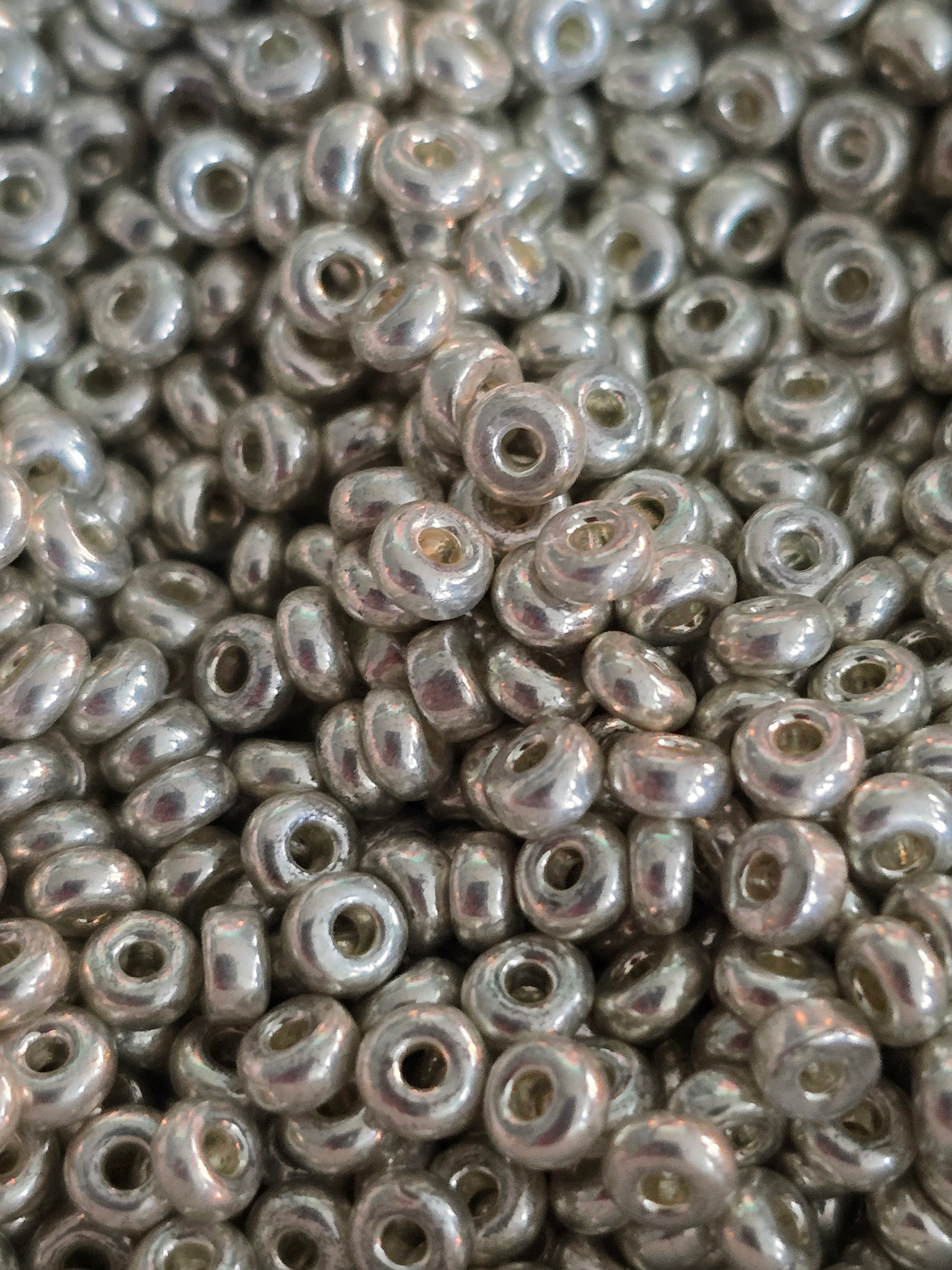 A close-up pile of small metallic silver glass seed beads with a glossy finish.