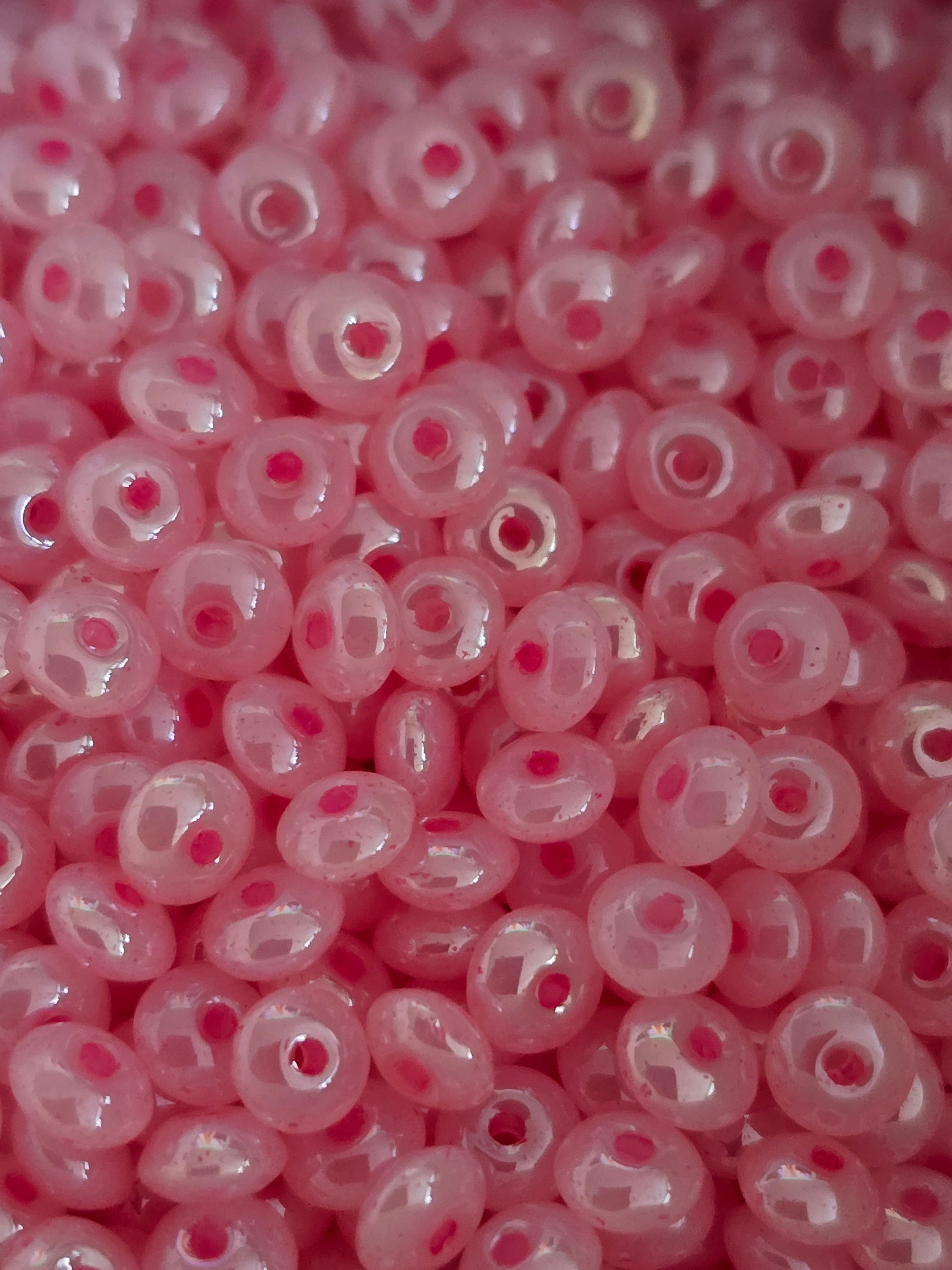A close-up view of many glass pink seed beads with center holes, filling the entire frame.