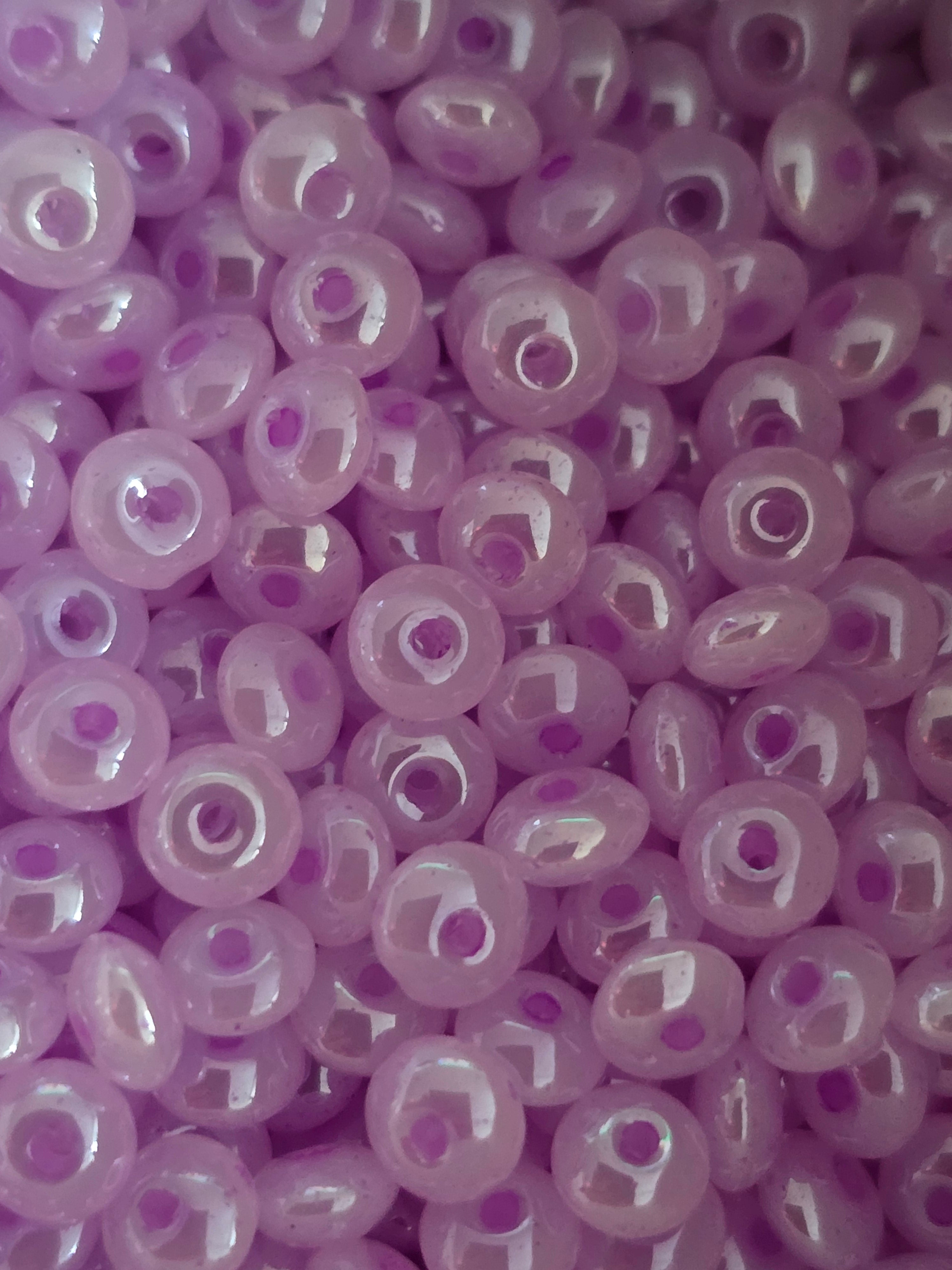 A close-up pile of lavender purple glass seed beads with a central hole, showing a glossy finish.
