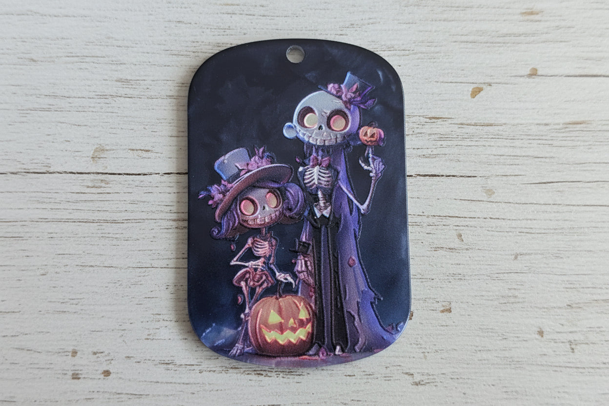 A dark, rounded rectangular with a small hole on the left, featuring a Halloween-themed illustration of skeleton characters and a glowing jack-o'-lantern 
