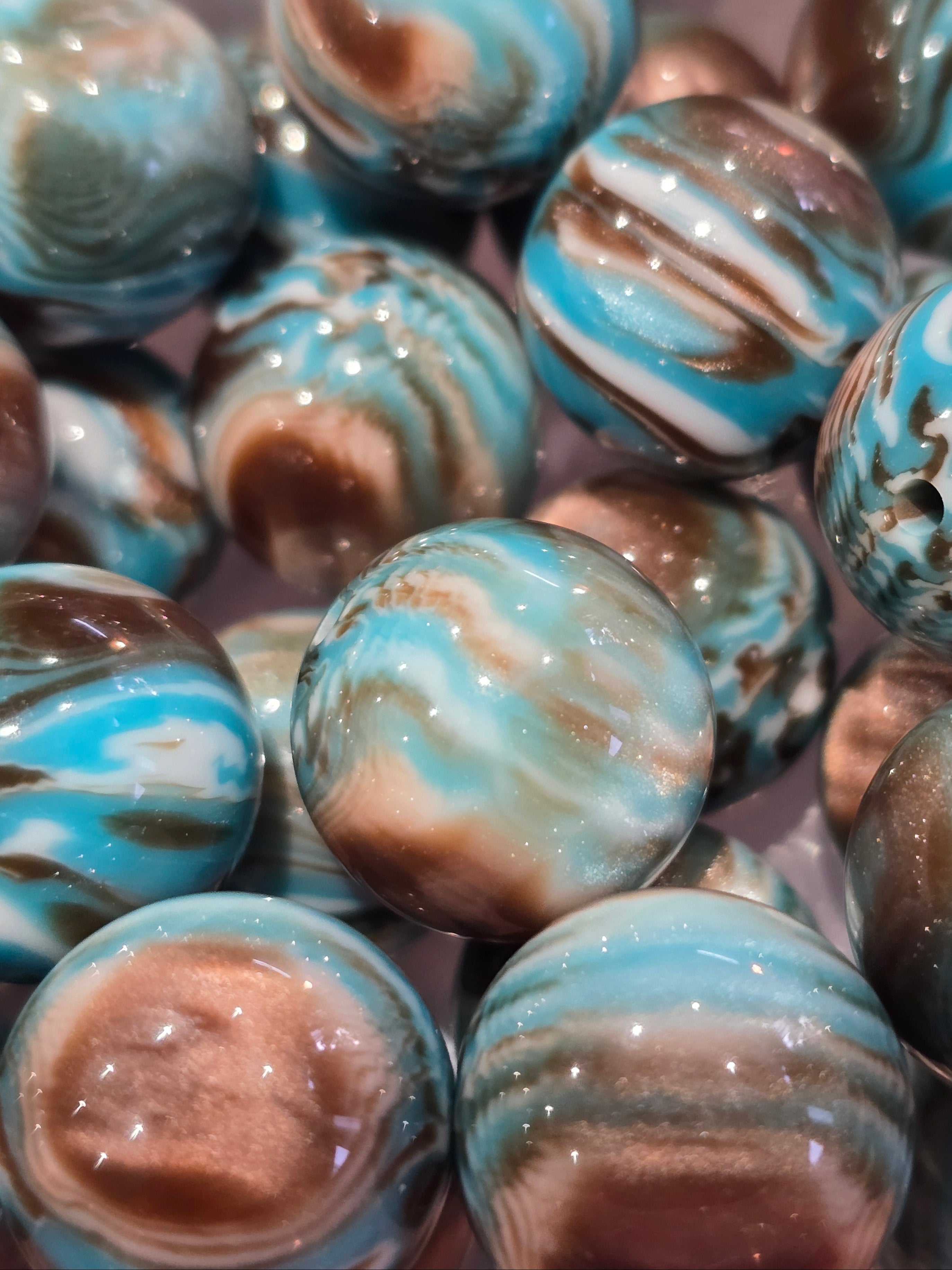 A close-up pile of glossy marbled  20mm beads with swirls of turquoise blue, brown, cream, and white.