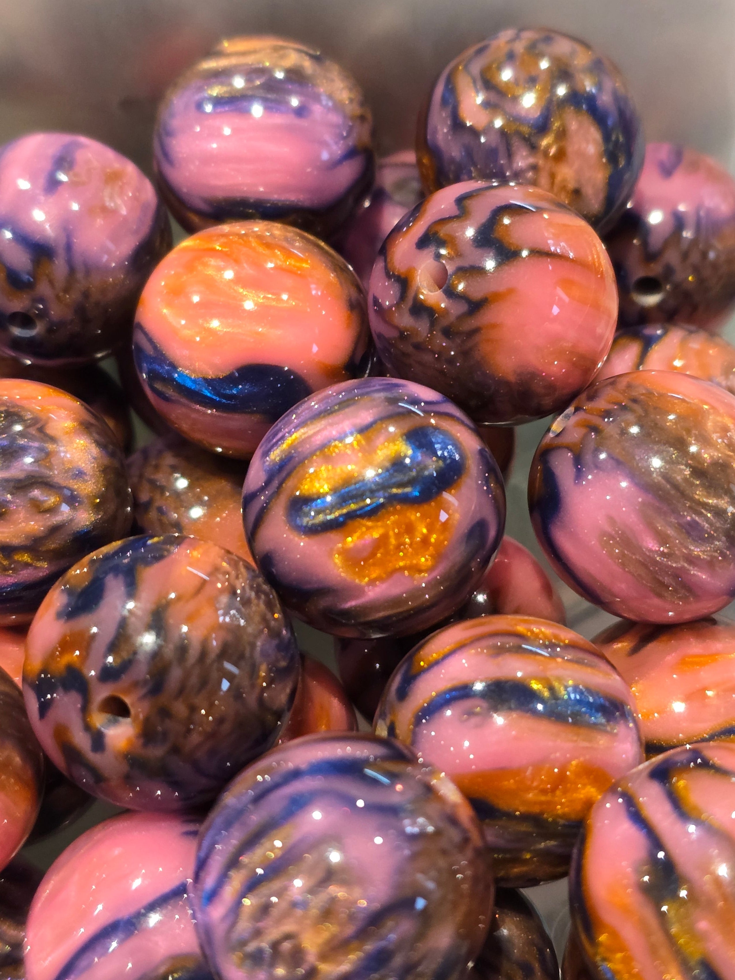 A close-up pile of round marbled beads with swirls of pink, purple, blue, orange, and gold in a glossy finish.