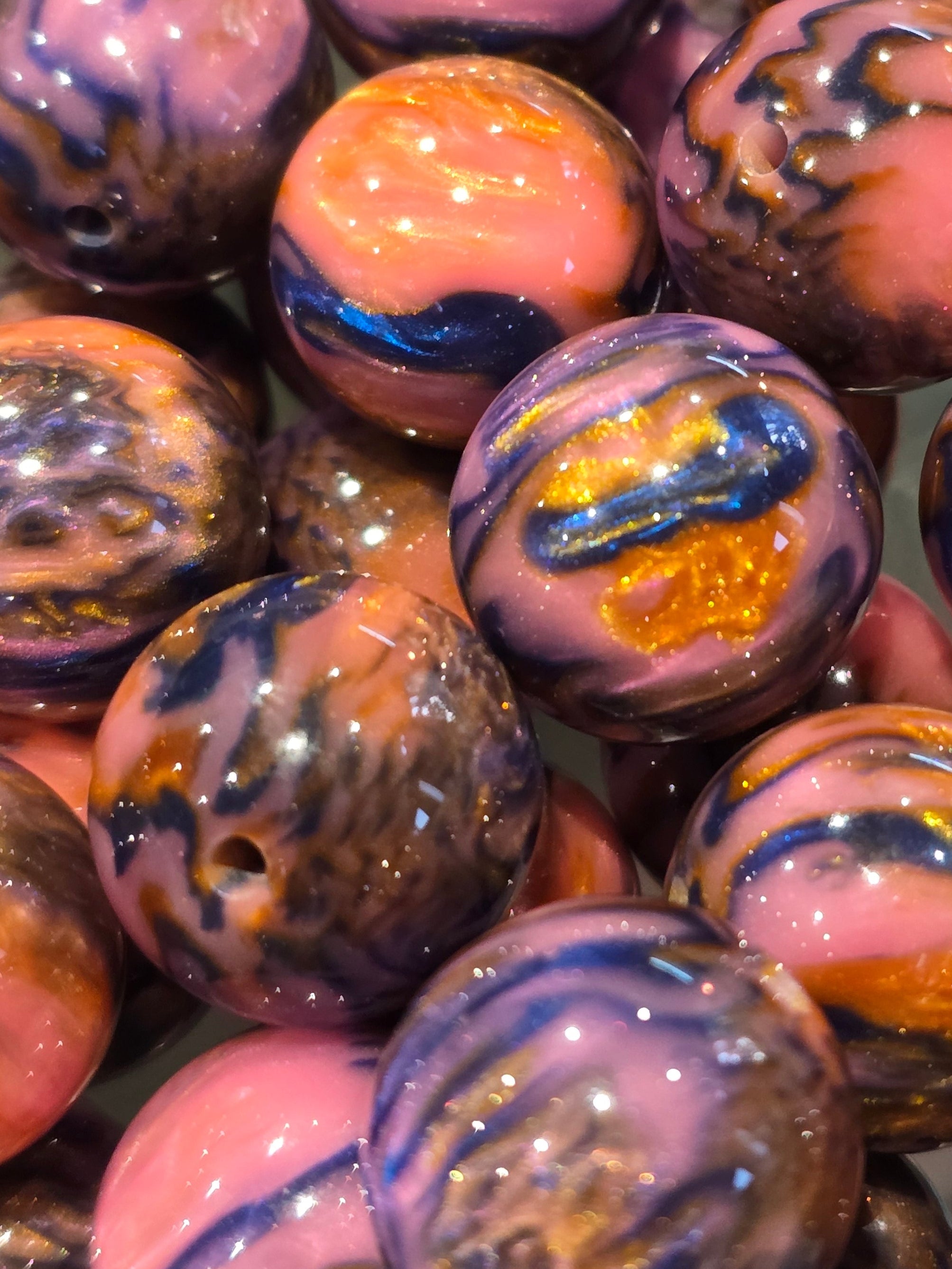 A close-up pile of round 20mm marbled beads with swirls of pink, purple, blue, orange, and gold in a glossy finish