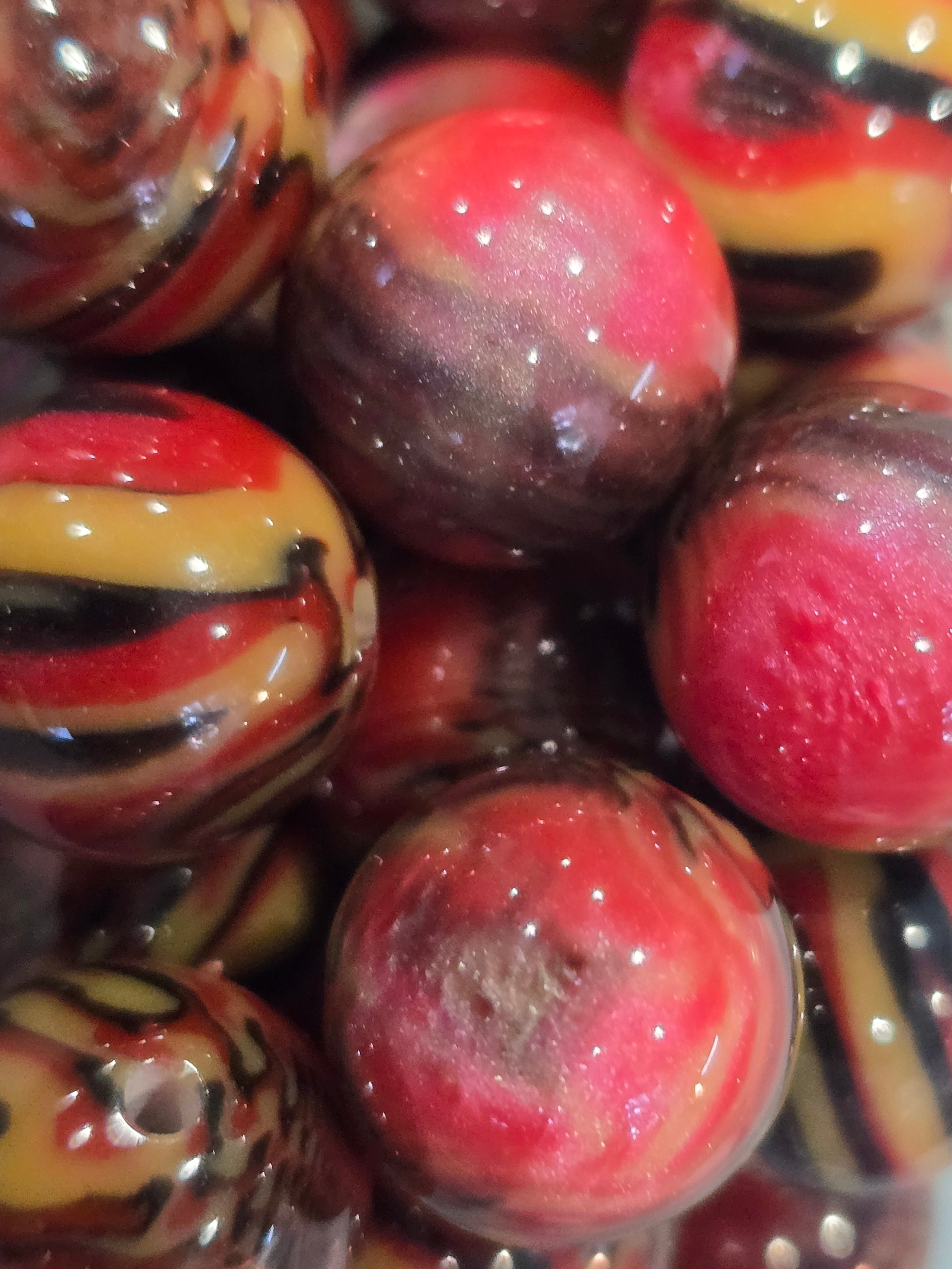 A close-up pile of glossy, round glass beads featuring marbled swirls of red, yellow, black, and brown.