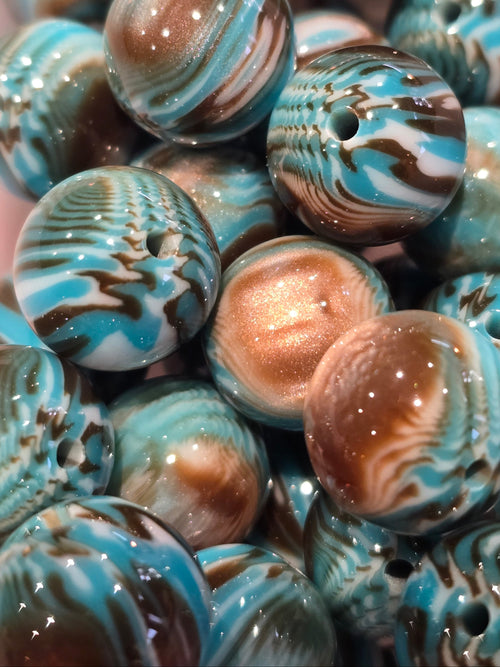 A close-up pile of round glass beads with a marbled swirl pattern in turquoise blue, brown, white, and metallic bronze.
