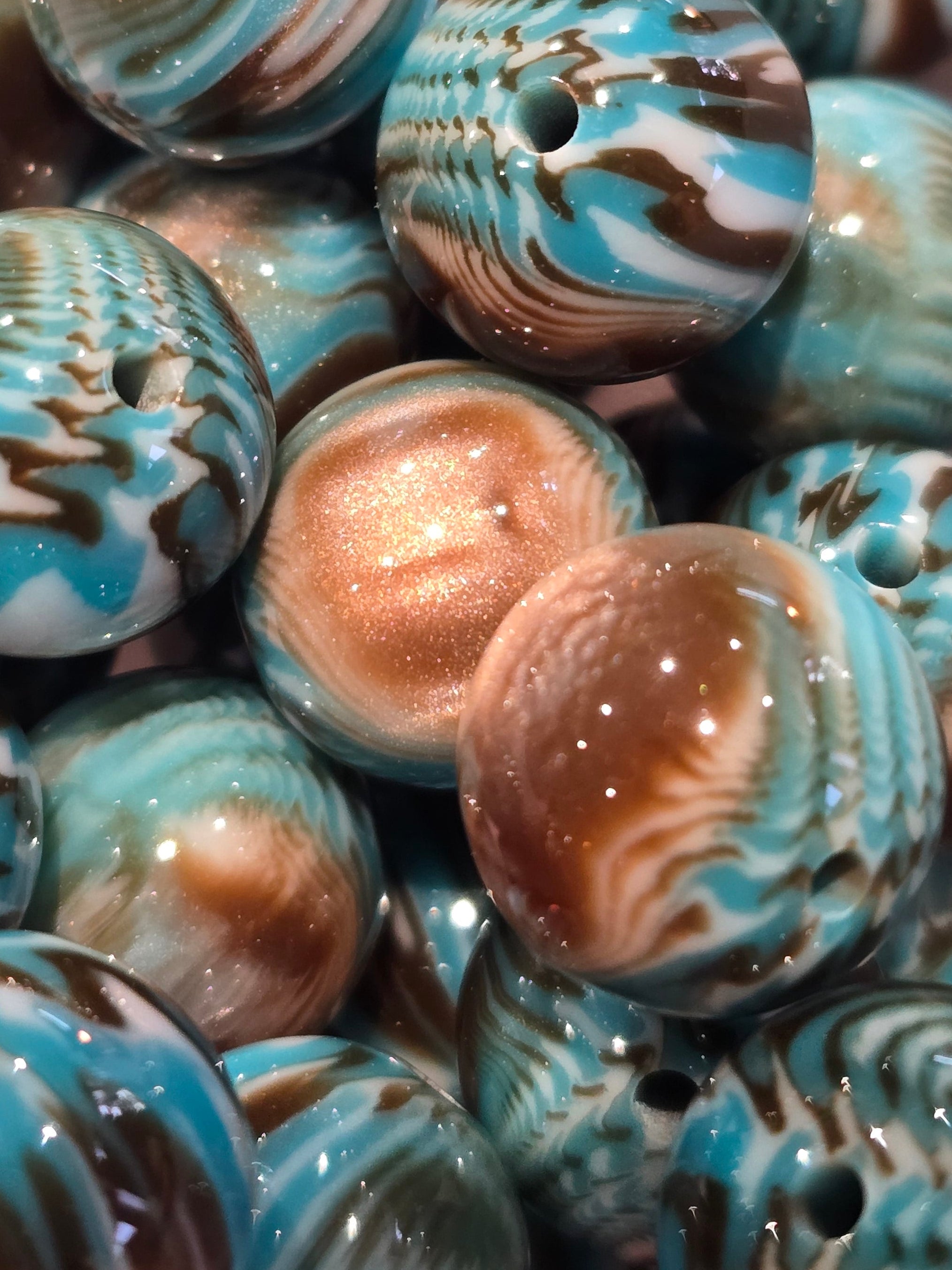 A close-up pile of round 20mm resin beads with a marbled swirl pattern in turquoise blue, brown, white, and metallic bronze.