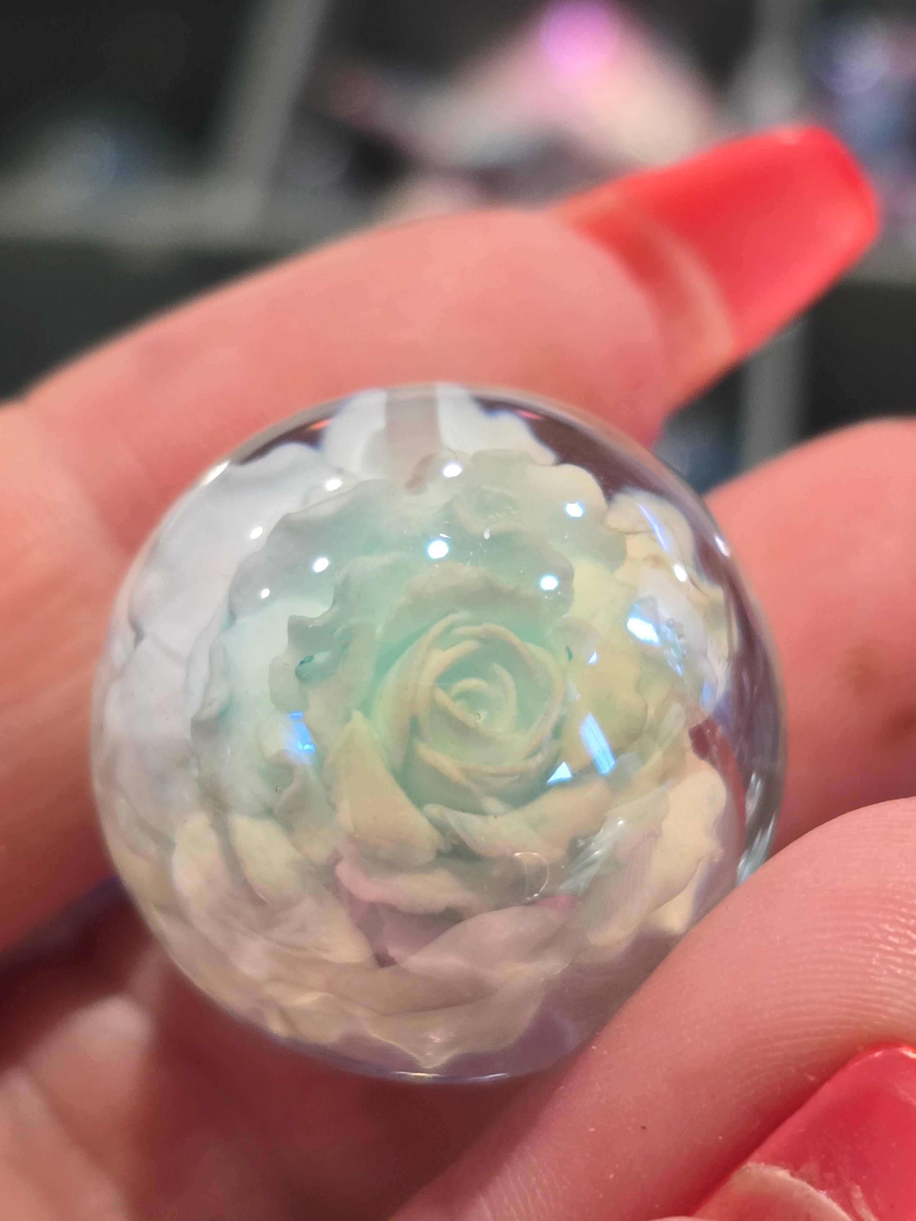 A close-up of a clear resin top hold bead containing a pale mint blue and white rose.