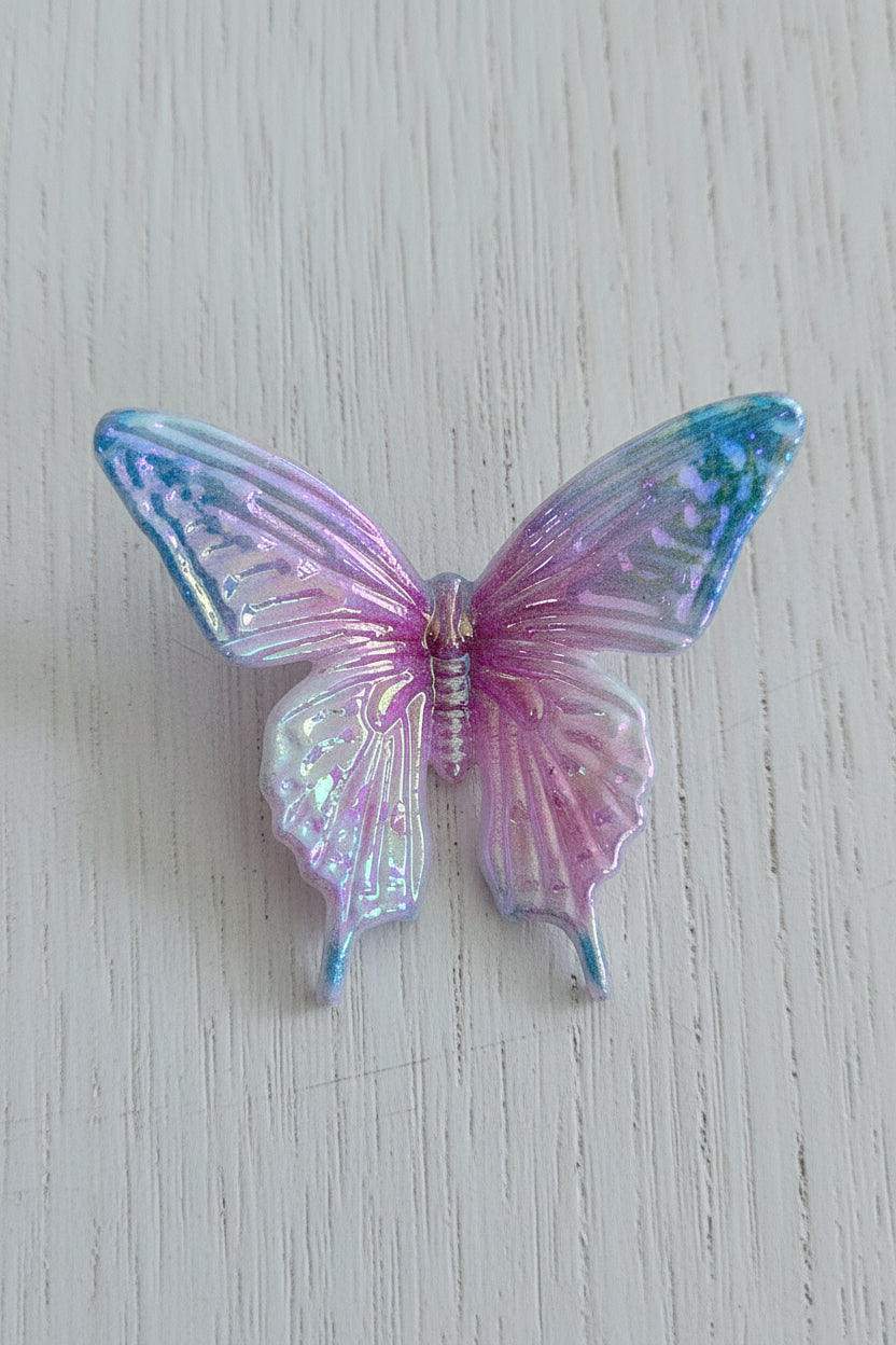 A butterfly-shaped acrylic bead with iridescent, holographic wings that transition from light blue to lavender and pink.