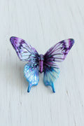 A small butterfly-shaped acrylic bead with iridescent purple, blue, and white wings.