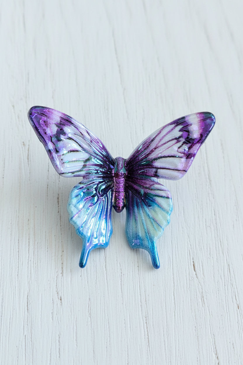 A small butterfly-shaped acrylic bead with iridescent purple, blue, and white wings.