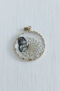 A round glass cabochon pendant featuring a white dandelion and a small dark butterfly, set in a gold-toned metal frame.