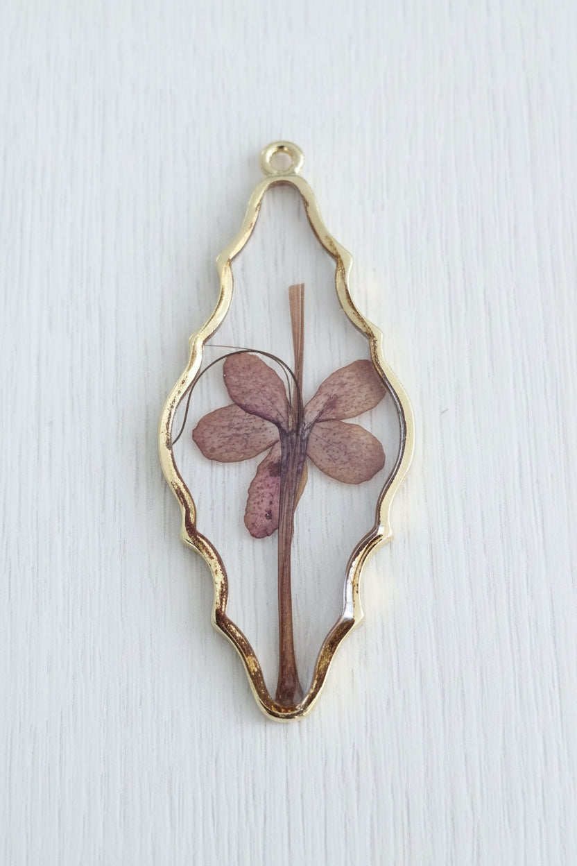A teardrop-shaped gold-toned pendant containing a preserved dried flower.