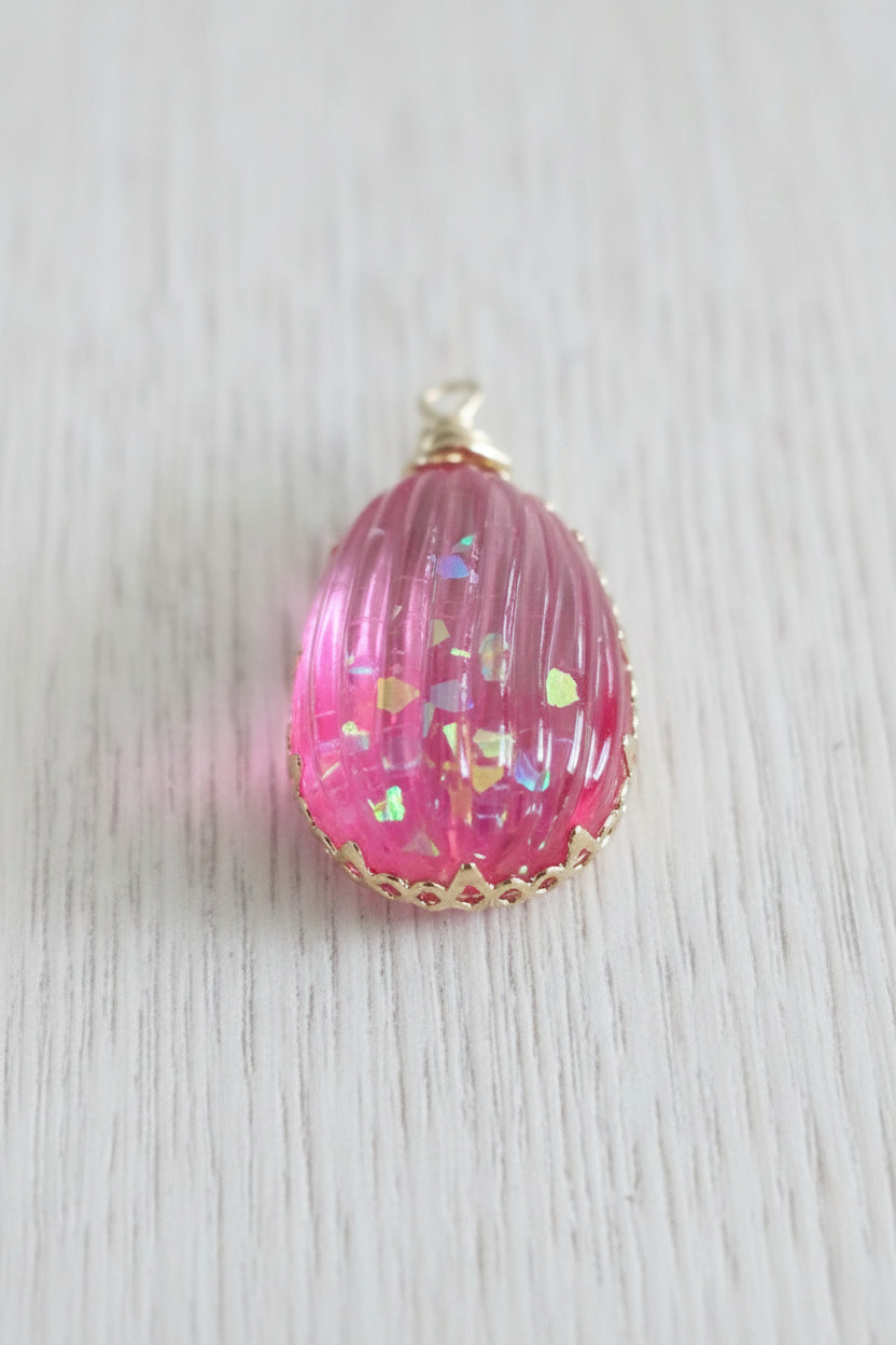 A pink teardrop-shaped pendant with a textured, ribbed surface containing iridescent glitter, finished with a gold-tone bail.