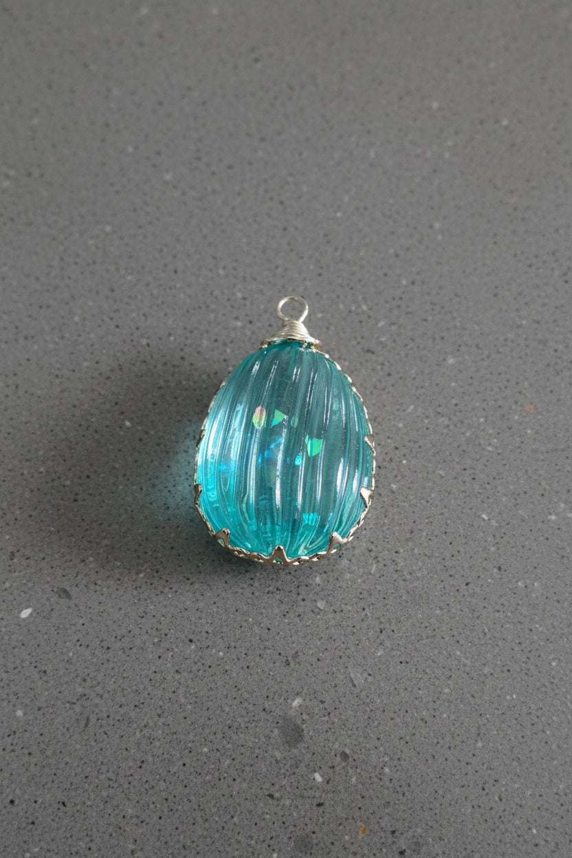 A teardrop-shaped turquoise glass pendant with a ribbed texture and a small gold wire bail.