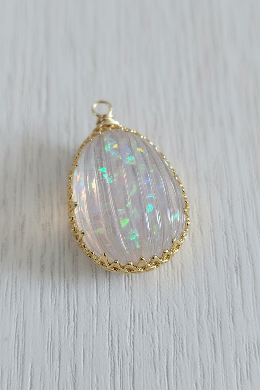 A teardrop-shaped pendant with a milky white iridescent opal inlay set in a gold-toned bezel.