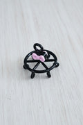 A small black metal wheel-shaped pendant with a pink bow accent.
