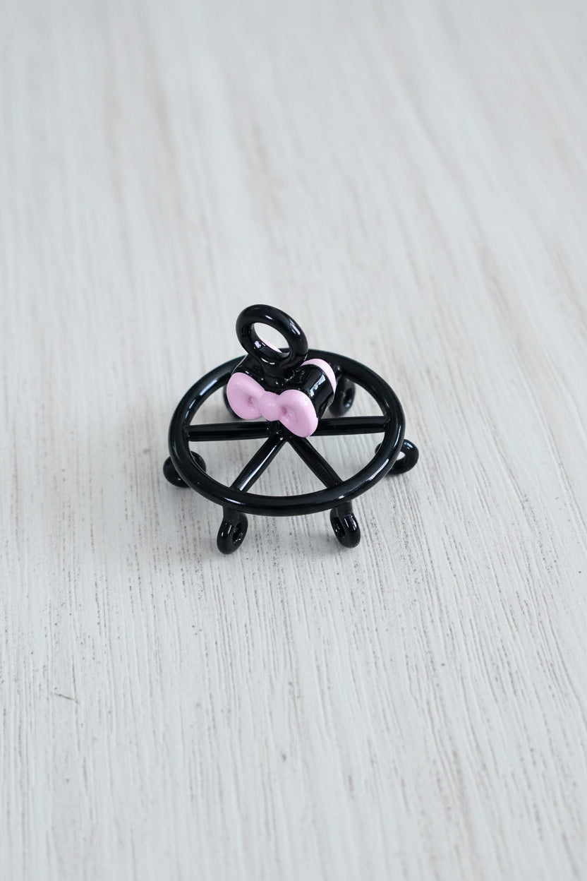 A small black metal wheel-shaped pendant with a pink bow accent.