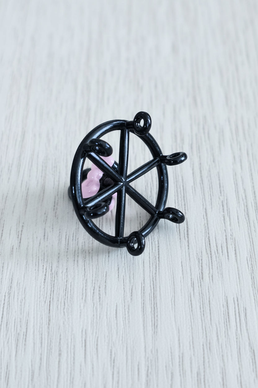 A small black metal wheel-shaped pendant with a pink bow accent. Underside view