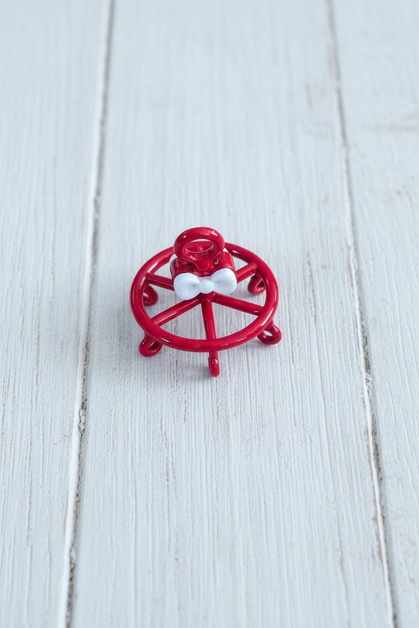 A small red decorative wheel charm with a white bow in the center