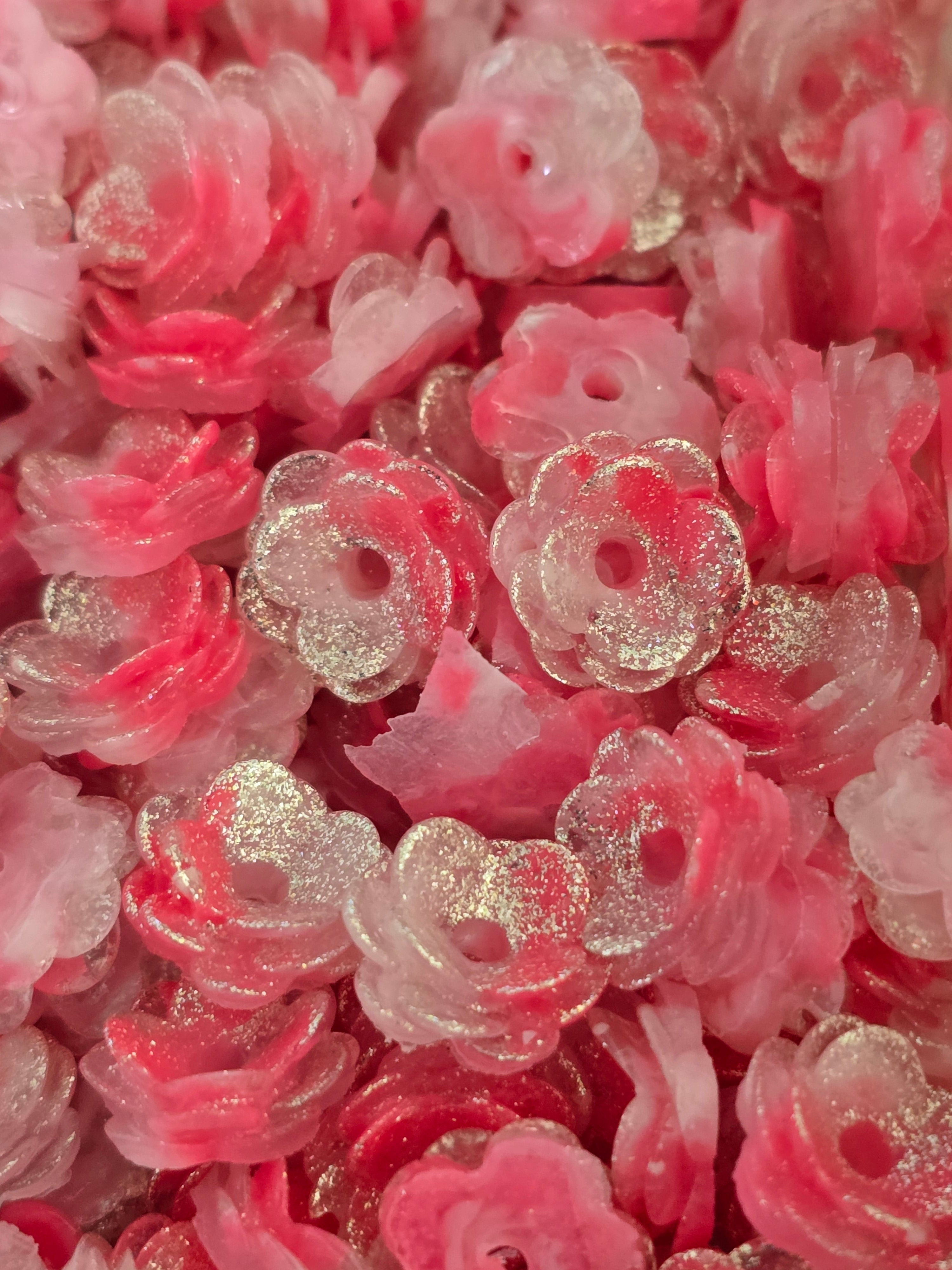 A close-up pile of small translucent pink and clear flower-shaped beads with a glittery silver finish.