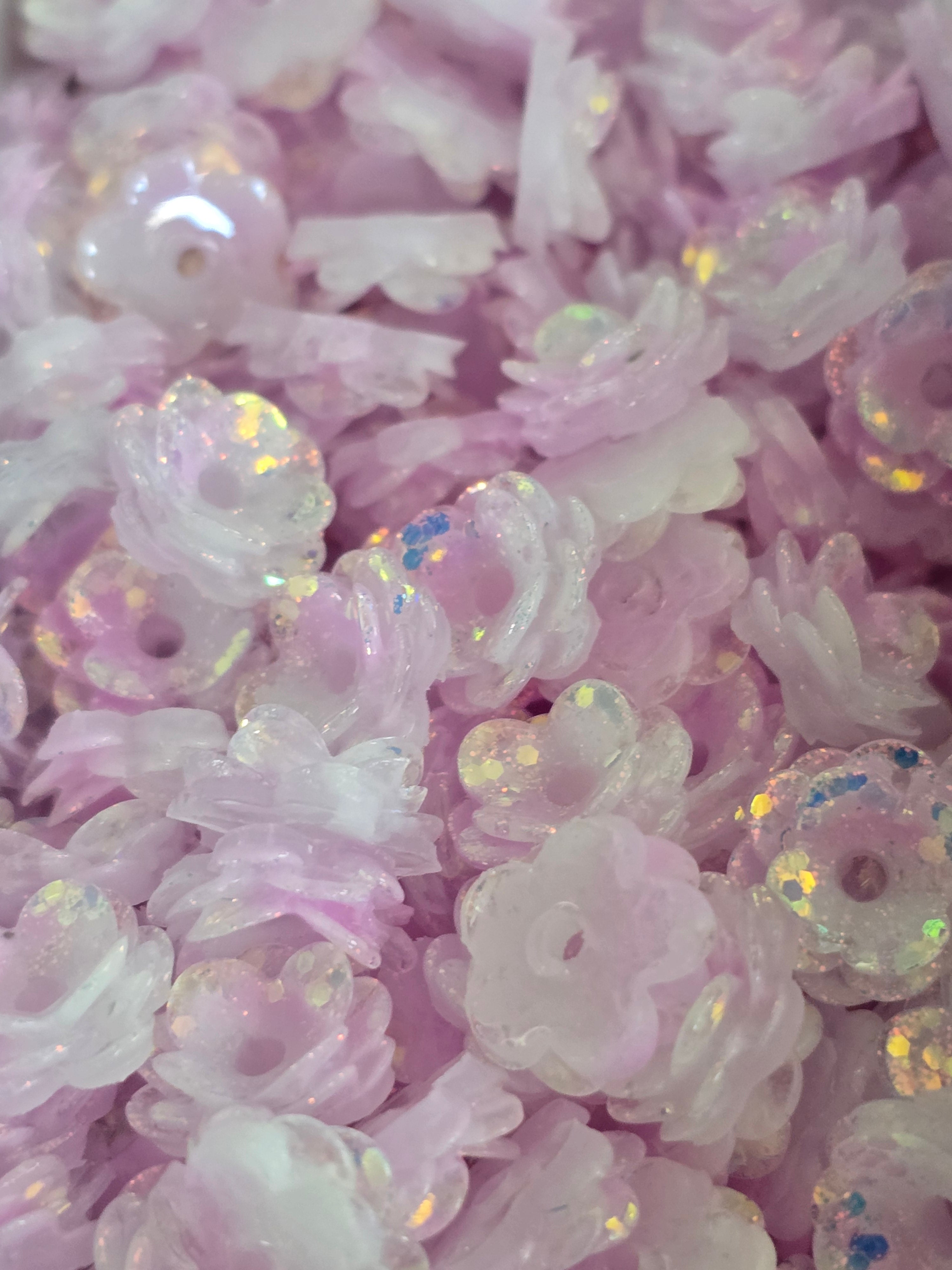 A close-up pile of small translucent lavender-pink flower-shaped beads with iridescent glitter.