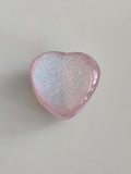 A heart-shaped pink resin bead with shimmering silver glitter, shown on a neutral light gray background.