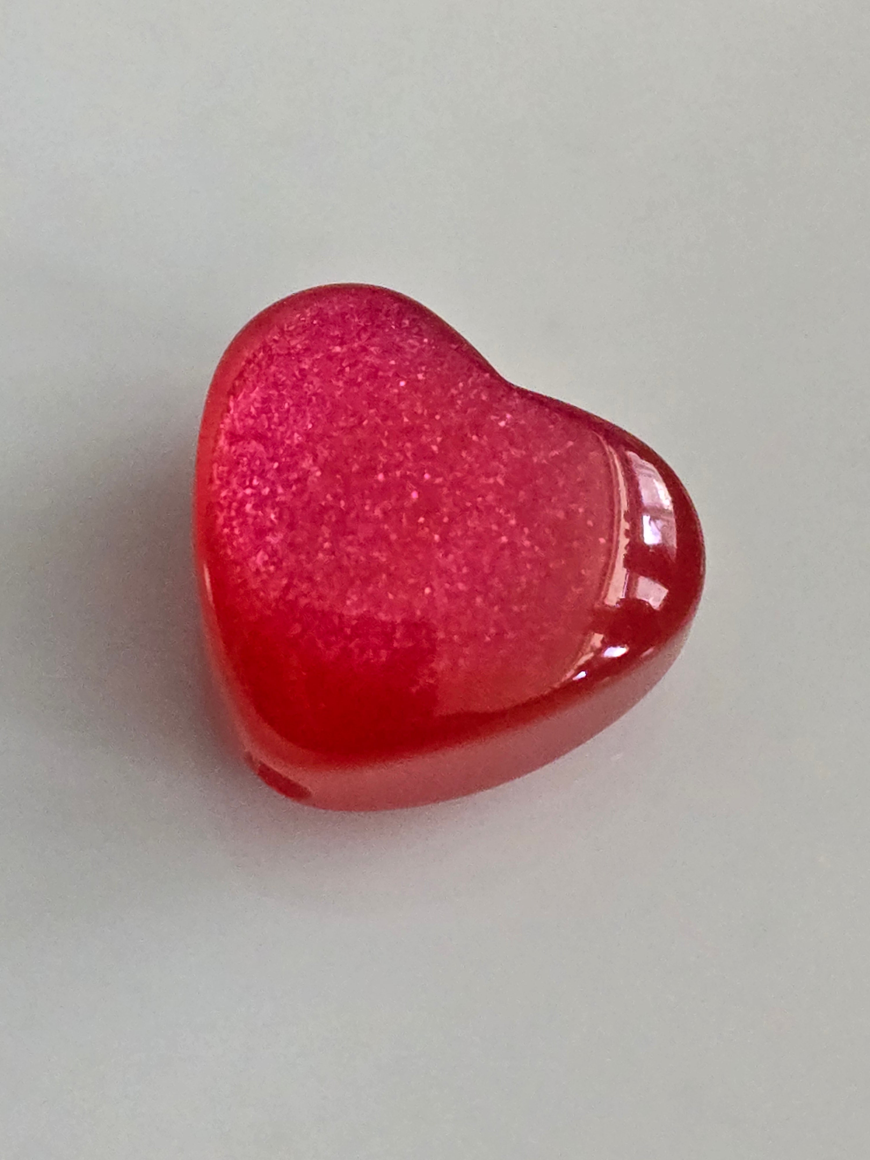 A small, heart-shaped red resin bead shown on a plain light gray background.